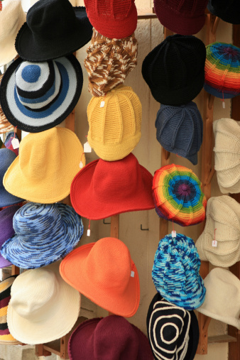 Close-up of many different colorful women's summer hats for sale on display at the local clothing store in France. Straw hats, as well as knitted hats, in various styles and colors, including yellow, red, orange, white, black, etc. Some hats have price tags hanging on them.