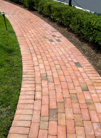 Curving Red Brick Sidewalk of American Luxury Home with mulched shrubs on the side