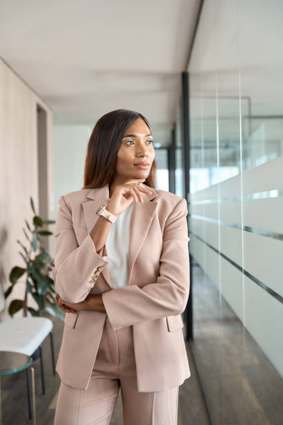 istock Young pensive business woman in office looking away thinking, vertical. 1572980030