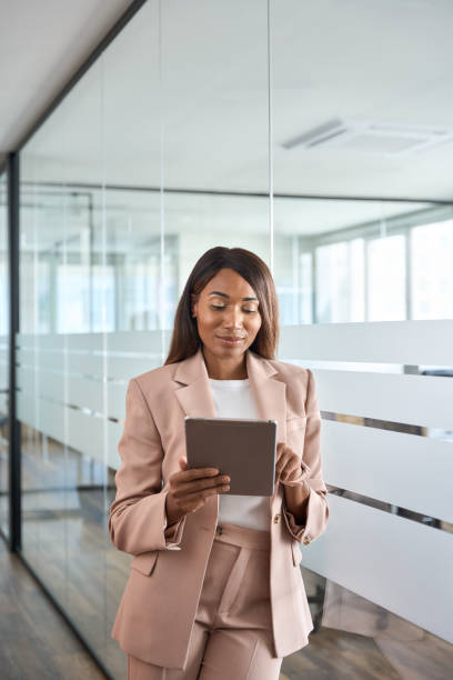 istock Young professional business woman using tablet standing in office, vertical. 1572980467