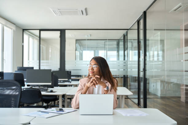 Smiling young businesswoman working on computer in office looking away.
