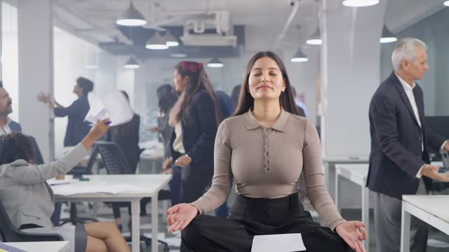 Indian corporate woman employee in meditative pose in chaotic office environment