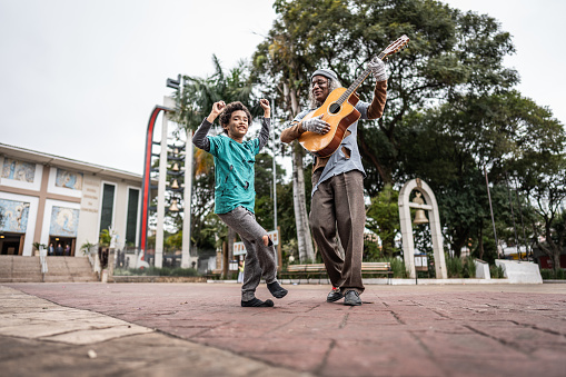 Senior homeless man playing music with a boy outdoors