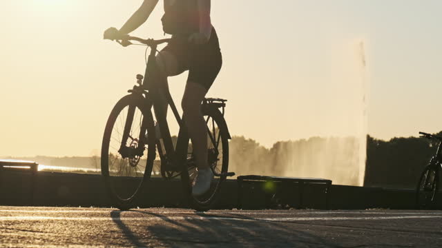 Silhouette of Woman on Bicycle Rides by Bike Path in Park at Sunset Slow Motion