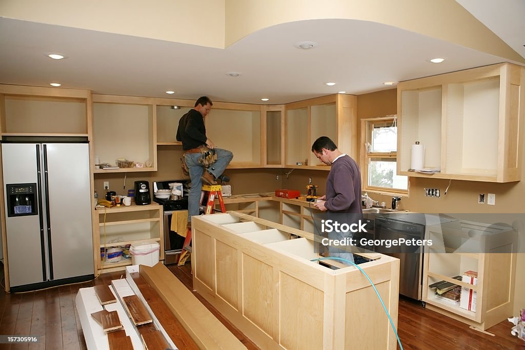 Kitchen Remodel Cabinet maker installing custom made kitchen island and cabinets, while electrician installs in-cabinet lighting. 

Very shallow DOF quickly drops off to nice soft focus. Home Addition Stock Photo