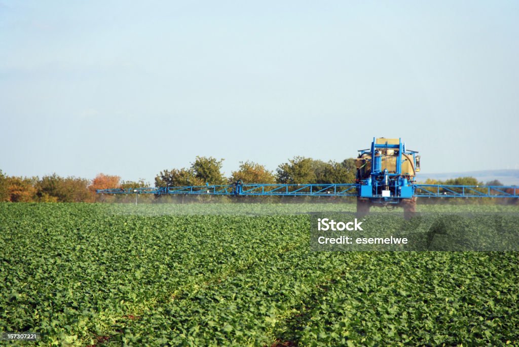 A farm sprayer distributes liquid chemicals to the crops  A tractor field sprayer spreading pesticide onto field Crop - Plant Stock Photo