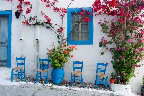 Four blue painted chairs standing in front of a typical white painted Greek village house on the island of Kos with bougainvillea