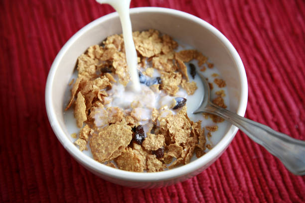 A hearty breakfast of cereal with milk Pouring milk into a bowl of whole grain cereal. Natural light. bran flakes stock pictures, royalty-free photos & images