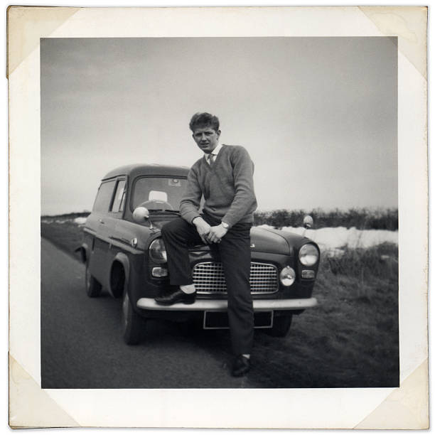 Black and white photo of man sitting on vintage car bonnet stock photo