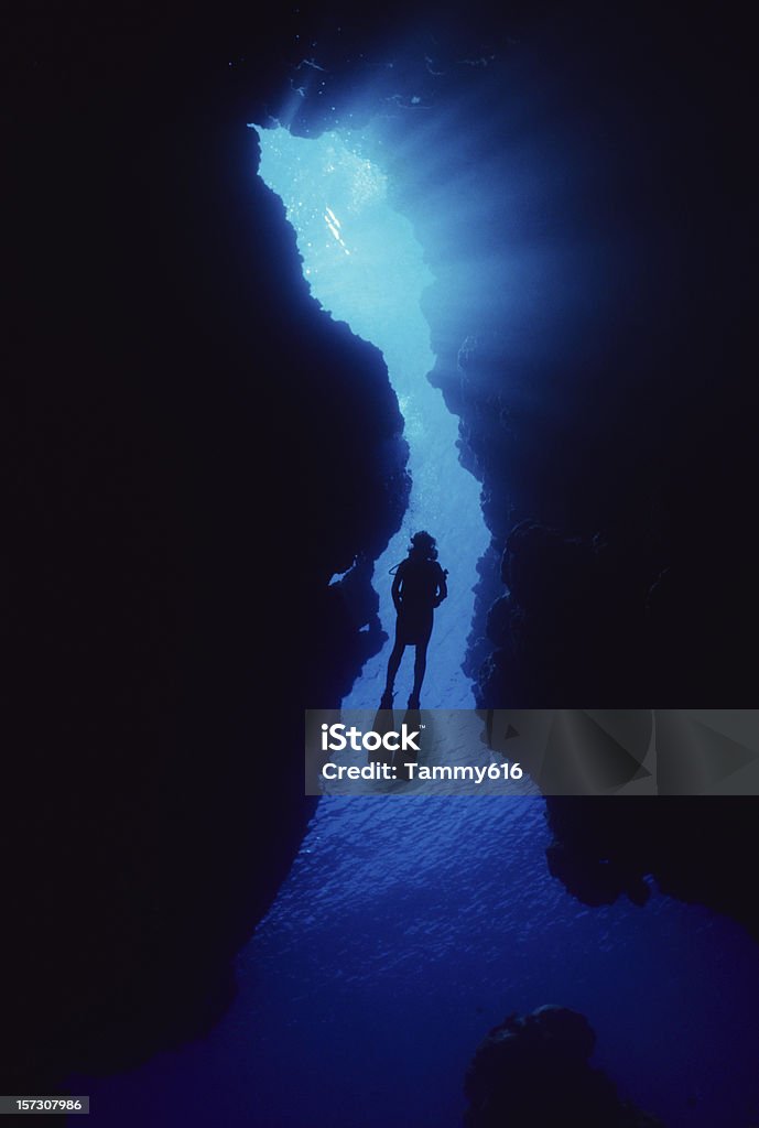 Woman In Cave Sun beaming through top of cavern. Underwater Diving Stock Photo