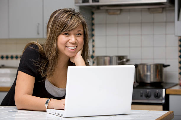 istock Asian Young Woman Smiling at Camera, Using Laptop in Kitchen 157308257