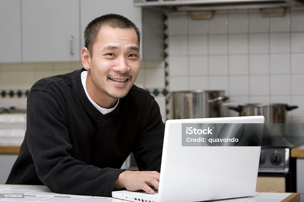 アジアの男性のノートパソコンにキッチン、笑顔でカメラ、Copyspace - ノートパソコンのロイヤリティフリーストックフォト