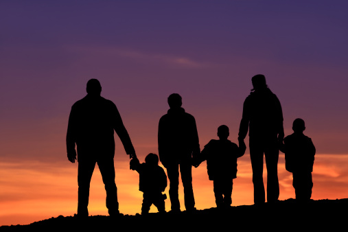 A silhoutte of a big happy family standing outside against dramatic sky. Two-generation family holding hands. Themes include bonding, love, relationships, togetherness, two parents, traditional family, father, mother, children, six people, four children, watching the sunset, back view, unrecognizable people. 