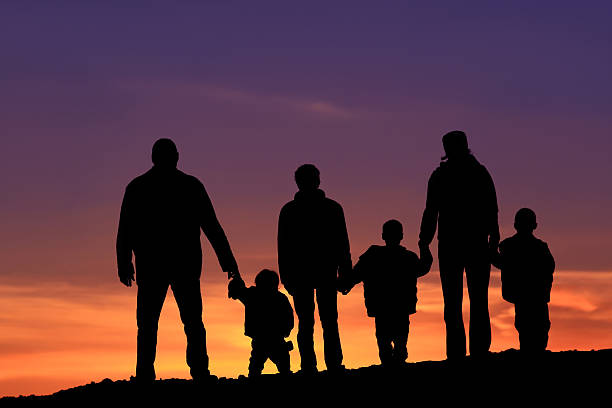 Silhouette of a Multi-Generational Happy Caucasian Family Holding Hands A silhoutte of a big happy family standing outside against dramatic sky. Two-generation family holding hands. Themes include bonding, love, relationships, togetherness, two parents, traditional family, father, mother, children, six people, four children, watching the sunset, back view, unrecognizable people.  line of people holding hands stock pictures, royalty-free photos & images