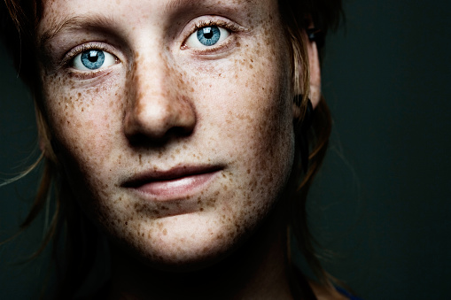 Portrait of a young girl with freckled skin and amazing blue eyes, slightly greenish in the background	