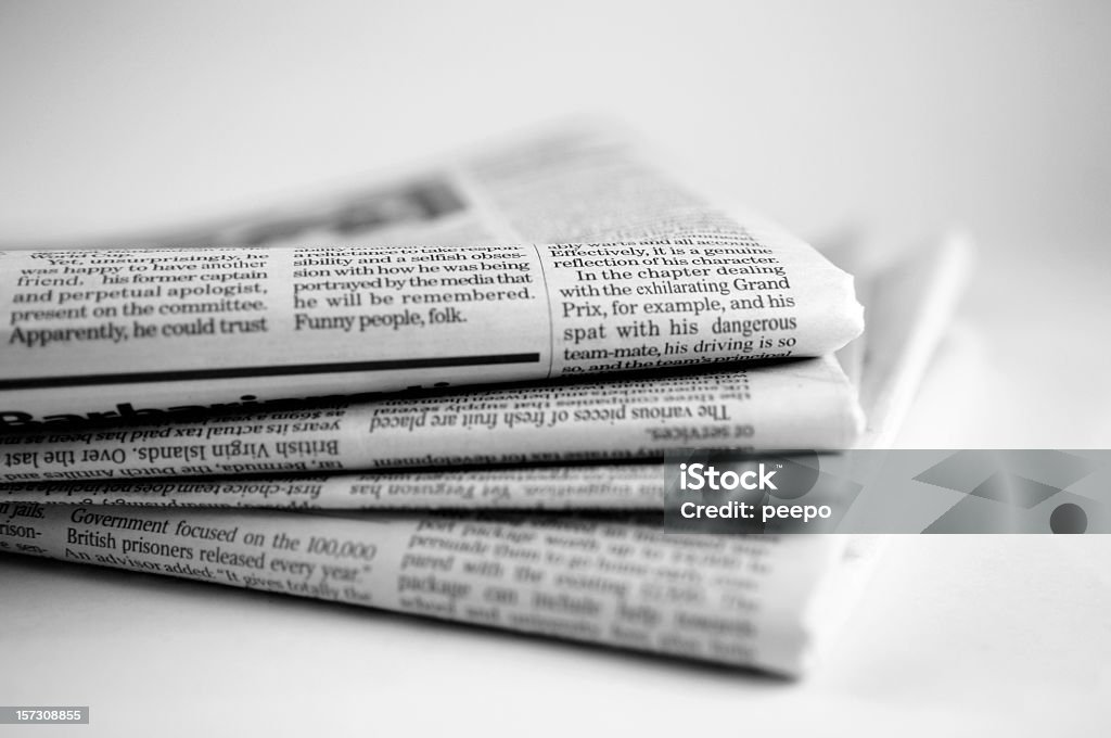 Newspaper Series A close up black and white image of a stack four broadsheet newspapers with English text, casually piled up on a plain white background. The macro image is shot with a shallow depth of field, with only generic text visible. With copyspace.   Newspaper Stock Photo