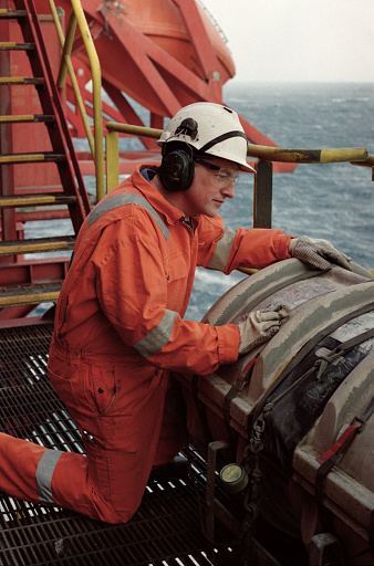 Roughneck, engineer or male technician working outdoors on a north sea oil drilling rig. Wearing safety equipment, coveralls, hard hat and gloves. Work, employment, occupation and oil industry are common themes.