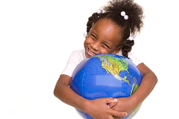 A child plays with a world globe ball by the sea in sunshine. Taken from a personal perspective viewpoint. The image is taken with a mobile phone for a modern style. This is a mass produced world sponge ball from a dollar shop, the map has been blurred. CONCEPT - Child with the world in his hands.