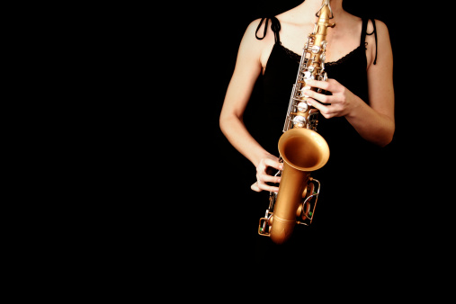A woman in an evening dress playing some jazz on the saxophone.  Just the sax and the player are visible; everything else has been intentionally darkened. Horizontal with plenty of copy space.