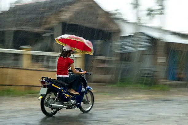 Photo of Vietnamese Woman Riding A Motorcycle While Holding An Umbrella