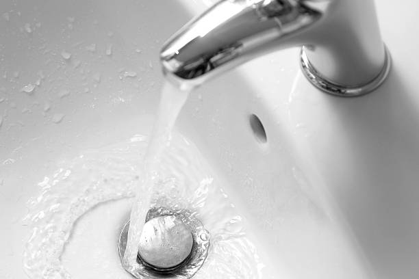 Close-up of sink and tap with falling water, bathroom interior, processed for black and white picture.