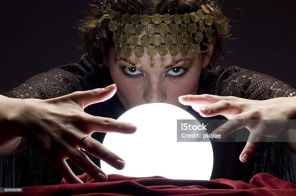 fortune teller with glowing crystal ball Close up of mysterious focused fortune telling woman wearing a copper hair dress with her hands on a glowing crystal ball looking at the camera Adult Stock Photo