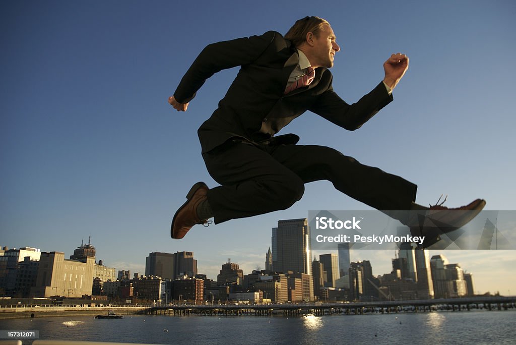 Businessman Jumping Over City Skyscraper Skyline Businessman gets a leg up on the competition, soaring over the financial district Businessman Stock Photo