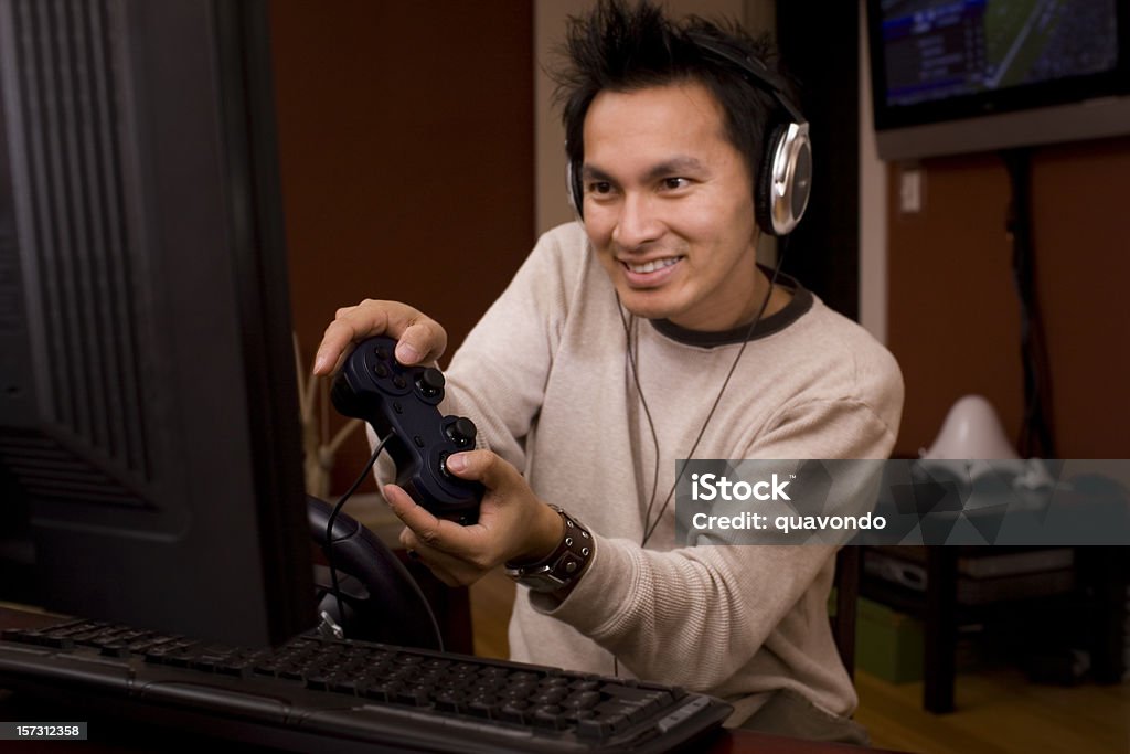 Asian Desktop PC Gamer Using Computer, Headphones, and Remote Control  Video Game Stock Photo