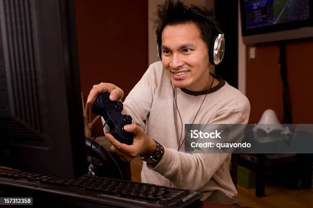 Asian Desktop Pc Gamer Using Computer Headphones And Remote Control Stock Photo - Download Image Now