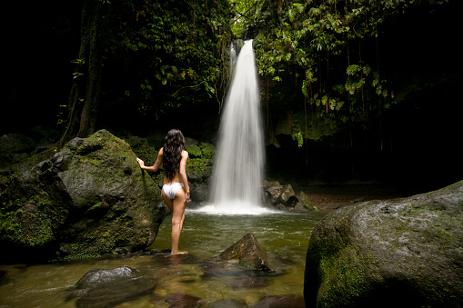 Girl in white bikini looking at the waterfall surrounded by the jungle.  Taken at Emerald Pool, Dominica.