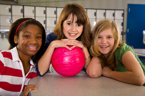 Three happy girls in a bowling alley with a bowling ball.