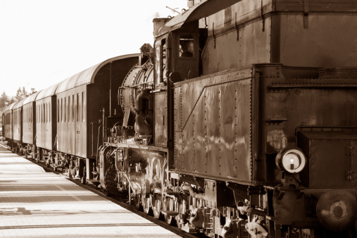 Mid 20th century locomotive steams through train station. Photo processed to sepia and slight grain for aging.