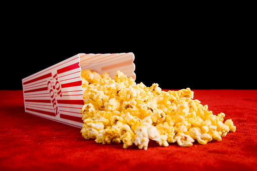 A bucket of popcorn spilling out onto the red carpet against a black background.