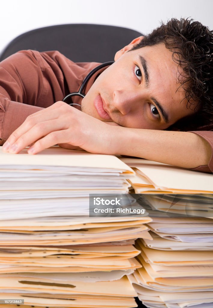 Exhausted Young Healthcare Worker A healthcare worker sitting behind a pile of paperwork. Exhaustion Stock Photo