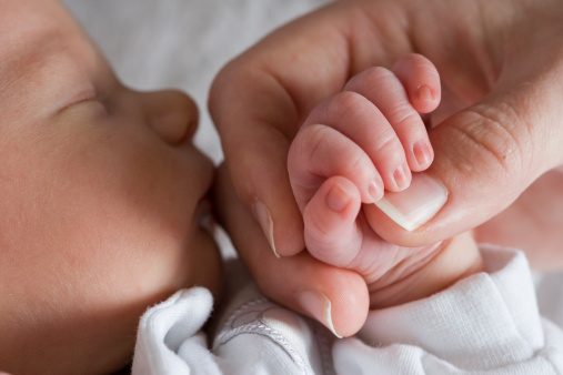 A newborn baby grasps his mother's hand.