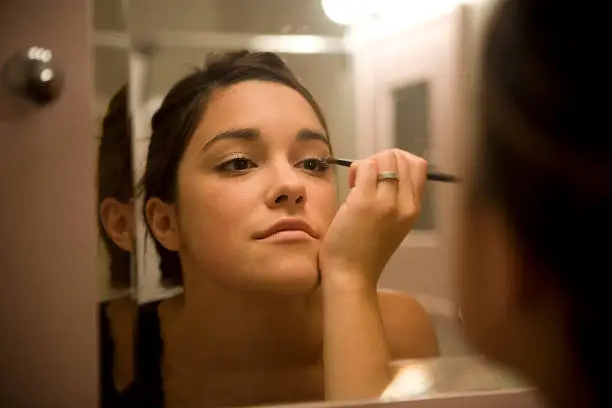 Young woman putting on her makeup in the bathroom mirror.