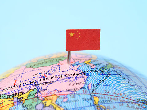 China flag pointing Beijing in cheap plastic globe. Shallow depth of field, focus on flag