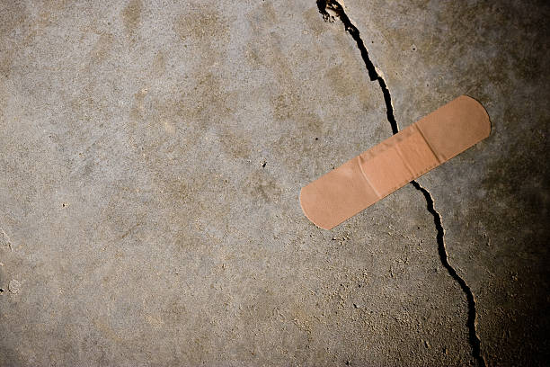 Crack in concrete with Band-Aid on top Adhesive bandage holding together a splitting concrete wall. (Concept: termporary solution) Tight/shallow DOF on bandage. stability stock pictures, royalty-free photos & images
