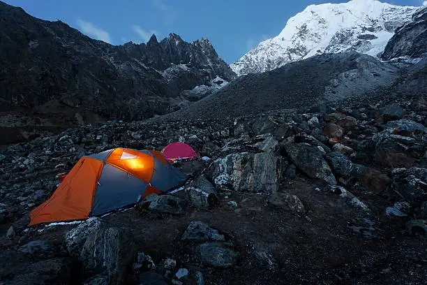 A tent with internal light at night below a very large mountain