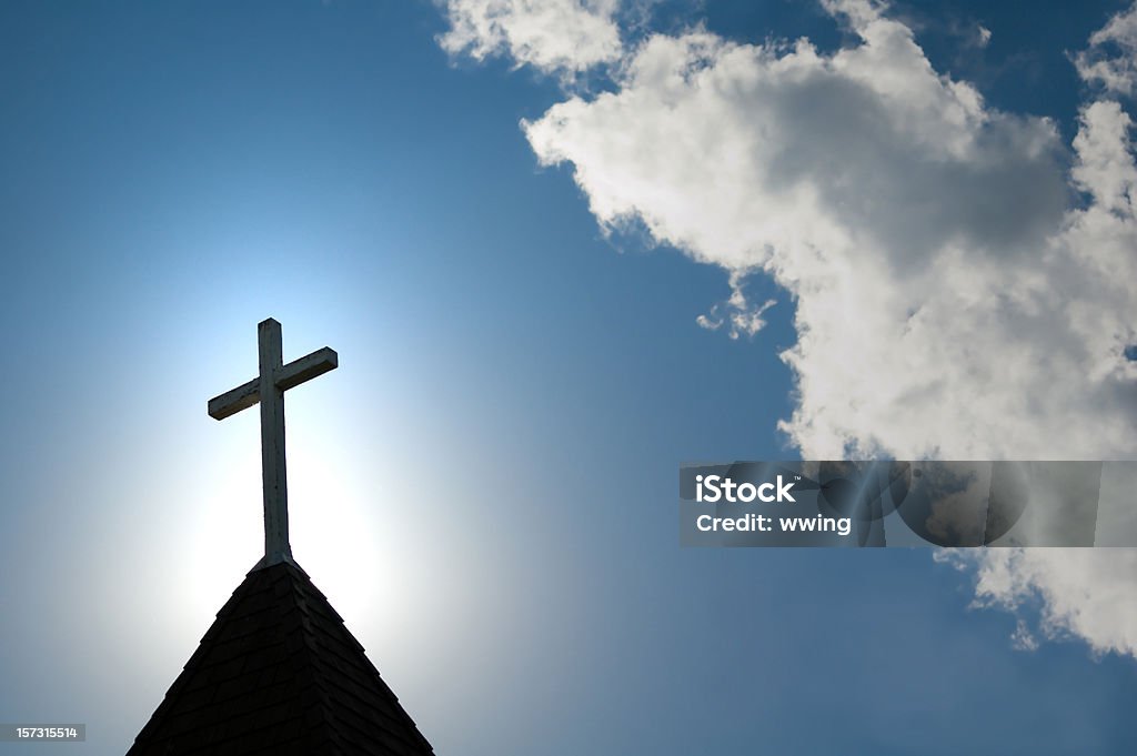 Easter morning with the sun behind a church steepl cross. A wood cross on an old church steeple backlighted by a rising sun. Some copy space. Church Stock Photo