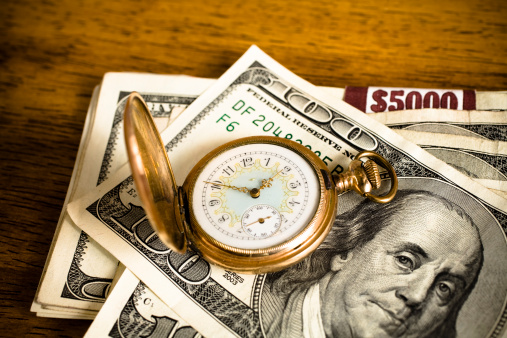 Anitque pocket watch on top of stacks of $100 bills.