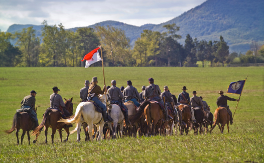 A troop of Confederate Cavalry ride across the battlefield at Cedar Creek in the Shenandoah Valley of Virginia during a reenactment.  The flag carried by the rider at the far right of the picture is the state flag of Virginia.