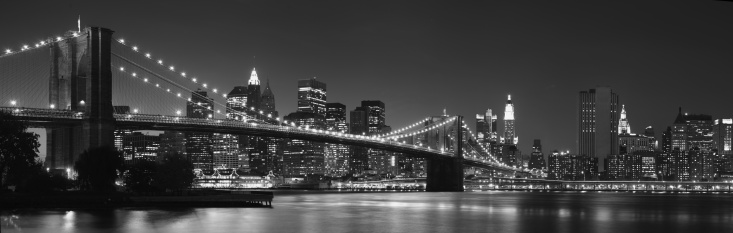 This is a horizontal, black and white, royalty free stock photograph of the New York City skyline viewed from Brooklyn. Manhattan buildings fill the lower part of the frame. A clear sky gives copy space. The iconic, landmark architecture, the Empire State Building stands taller than the other urban city structures. Photographed with a Nikon D800 DSLR camera.