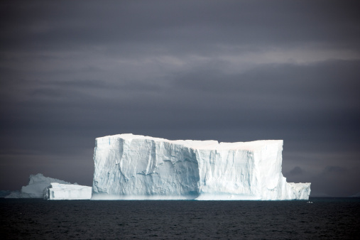Iceberg drifting in the Antarctic Ocean, dark grey stormy cloudscape. Antarctia.