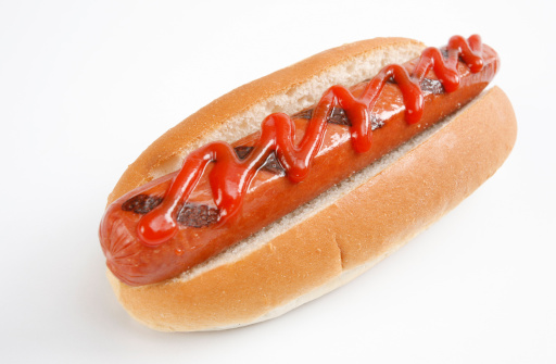Hot dog grilled sausage in a bun with sauces, on old dark  wooden table background.