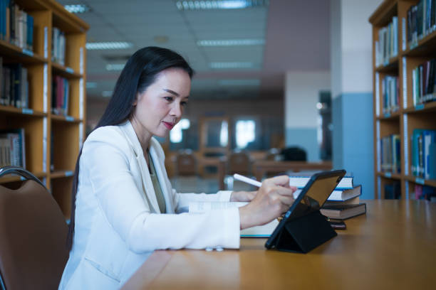 istock Female university lecturer working in library with a tablet and books on table 1573176748