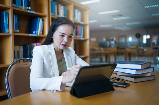 Female university lecturer working in library with a tablet and books on table