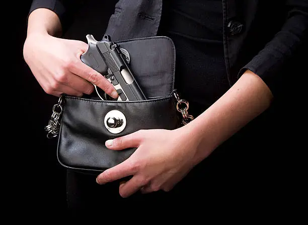 A close-up of a woman holding a handgun in a purse.