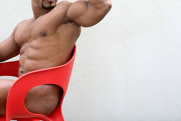 athletic male muscle nude in red chair stock photo