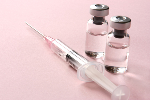 This is a studio shot of two glass vials with medicine and a single syringe ready for an injection or vaccination on a light pink background with copy space. The vials and syringe could represent various healthcare and medicine concepts.